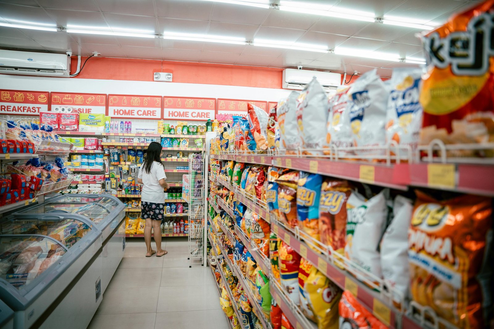 A woman browsing snack shelves at a supermarket, surrounded by various chips packages.